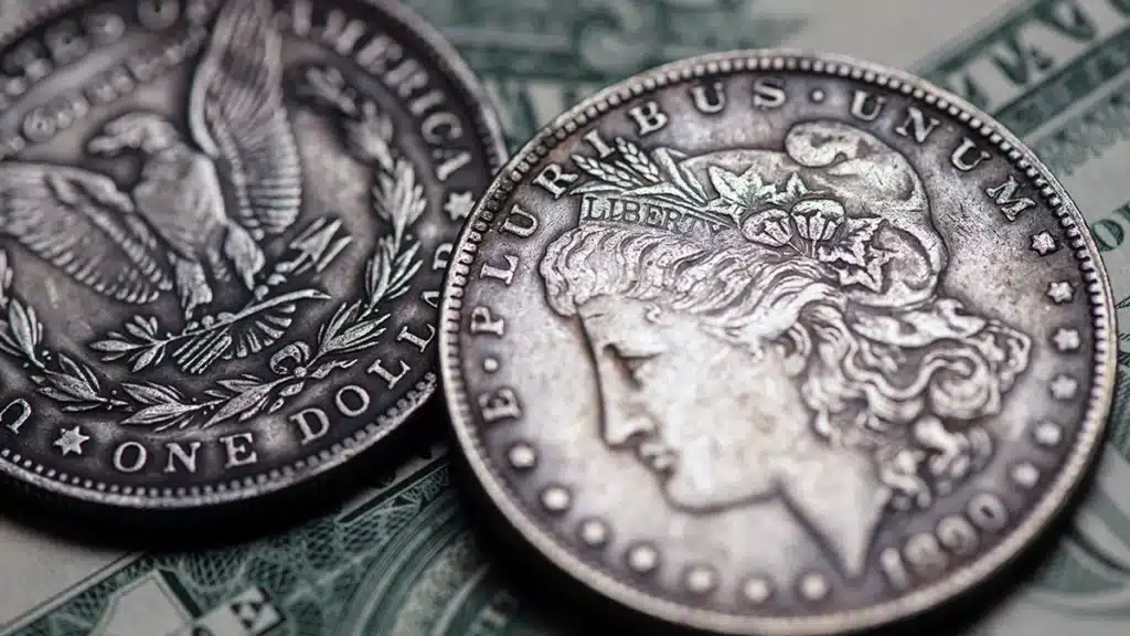 Two circulated Morgan dollars on top of a pile of one dollar bills. Image: Adobe Stock.
