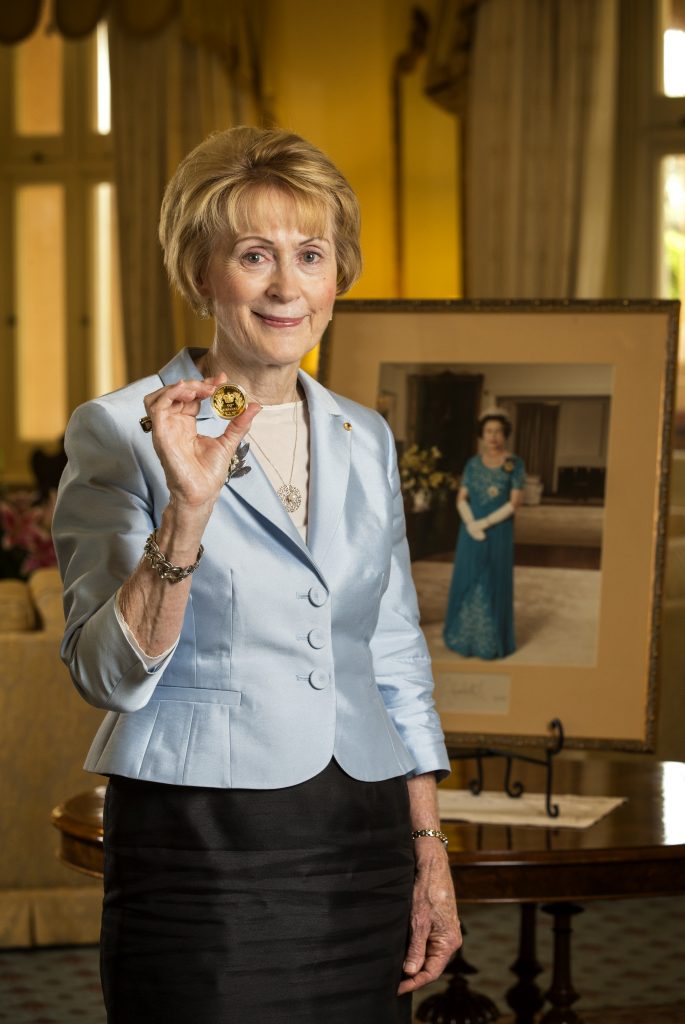 Her Excellency the Honourable Kerry Sanderson AO, Governor of Western Australia pictured in Government House holding the H.M. Queen Elizabeth II 90th Birthday 2oz Gold Proof High Relief Coin, in front of a portrait of Her Majesty. 