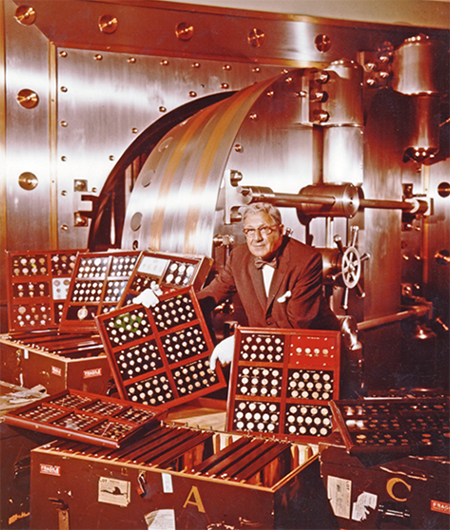 Louis Eliasberg, Sr. poses with his coin collection in front of a bank vault.