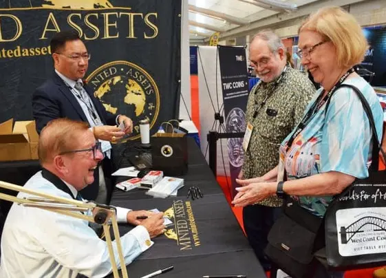 Minted Assets Founder and President Chang Bullock (standing left) and ANA Planned Giving Officer Thomas Uram (sitting left) greet show visitors as they hand out the free copper commemoratives.